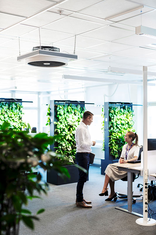 Ilmanpuhdistin, viherseinät ja kaksi työntekijää toimistossa